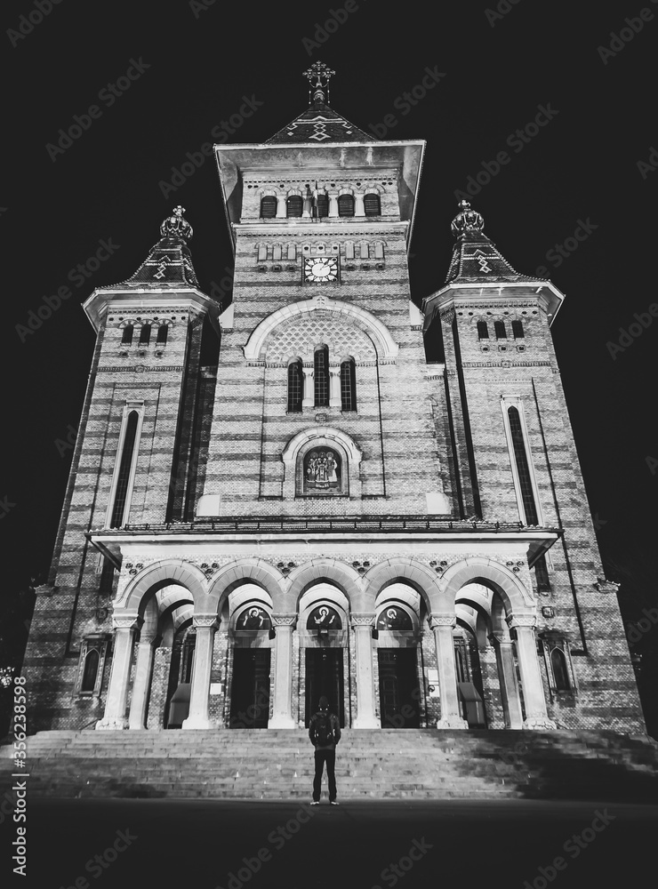 Fine art image of Orthodox cathedral in Timisoara with tourist standing in front of the entrance and looking up. Confession and religion in modern world.