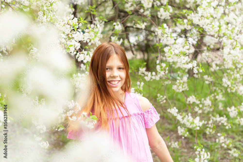 red-haired teen girl having fun in a blooming cherry orchard, the concept of spring and the end of the quarantine