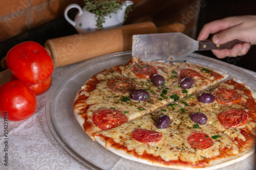 Margarita pizza, cheese with tomato sauce, with blurred background of tomato dough roll and hand holding cutting spatula