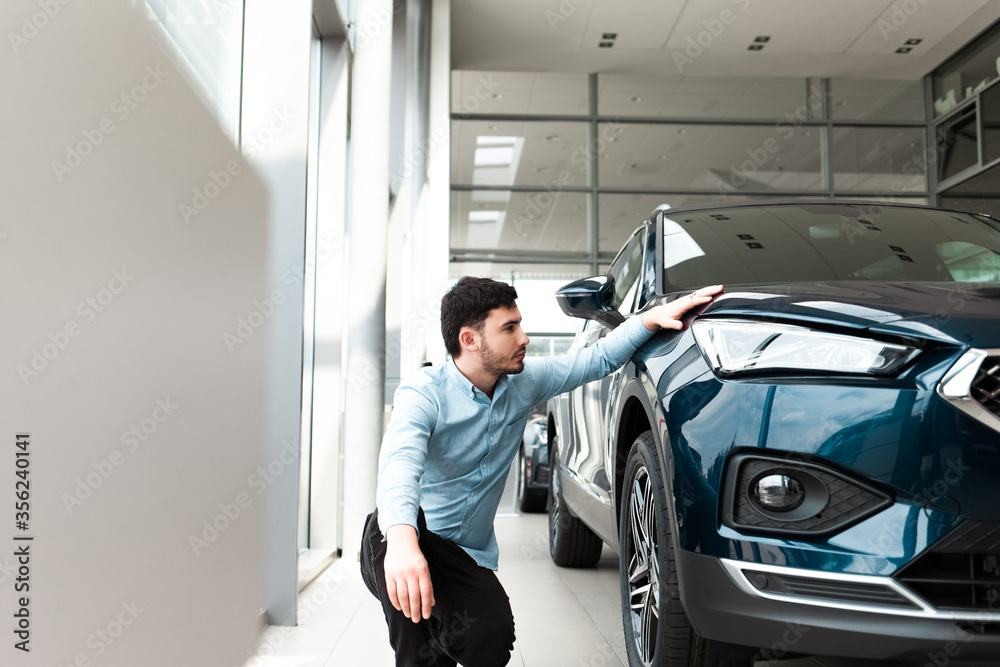 Man holds hand on his new car in a dealership Man holds hand on his new car in a dealership