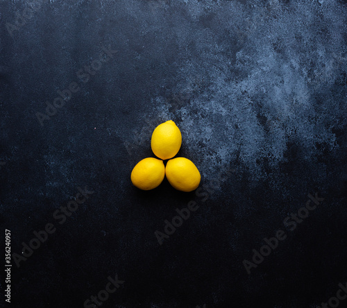 Deep dark blue painted surface that has light blue scuffs. Three lemons placed in the centre 