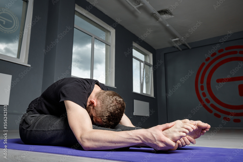 Young man doing leg stretching exercises on a yoga mat in the gym. Young man doing leg stretching exercises on a yoga mat in the gym.