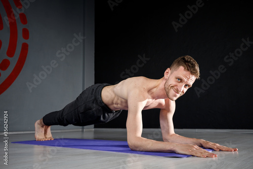 Younf athletic man is standing in forearm plank on yoga mat.