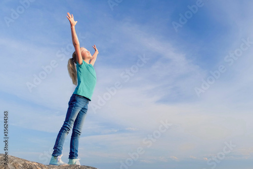 Relaxed girl breathing fresh air raising arms over blue sky at summer. Dreaming, freedom and traveling concept.