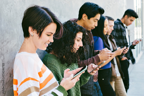 Canvas Print Group of young adults stare at their cell phones while standing against a wall i