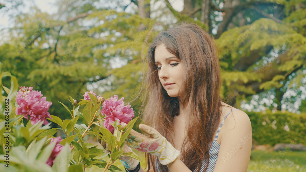 Portrait shot of cute young adult woman gardening flower plant in home garden relax rest outdoor in backyard grass, outdoors activities in sunny day in spring summer season. blurred background
