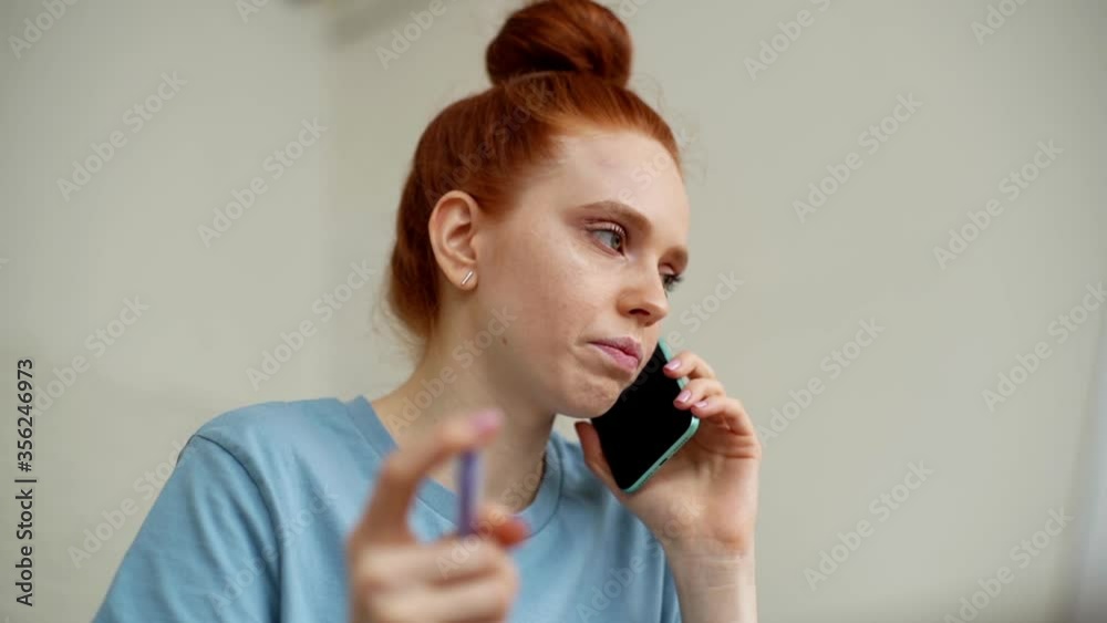 Close-up of face of concentrated redhead young woman talking on mobile phone at home office, view from below. Freelancer female is communicating with client by cell. Shooting in slow motion, Close-up of face of concentrated redhead young woman talking on mobile phone at home office, view from below. Freelancer female is communicating with client by cell. Shooting in slow motion,