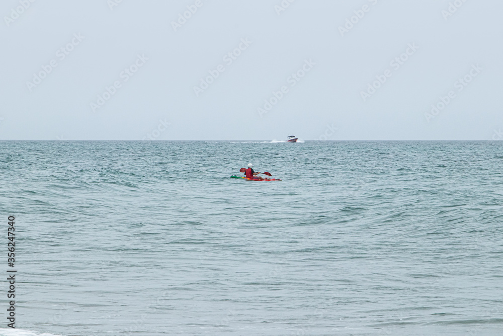 Kayaker in the ocean with motorboat in the distance
