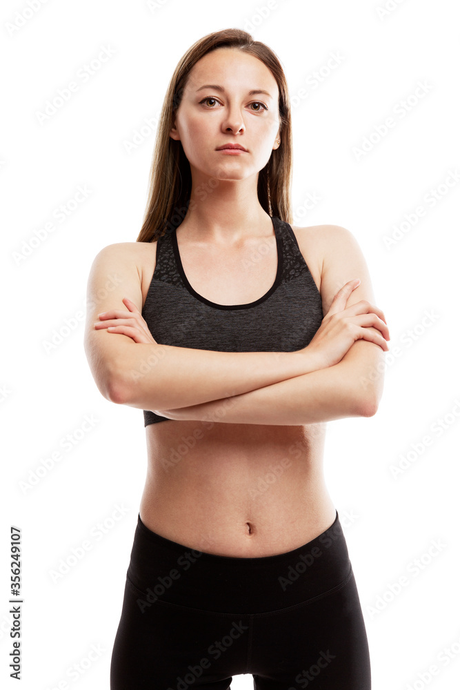 A serious slender young girl in sportswear is standing with her arms crossed on her chest. Sport and health. Isolated on a white background. Vertical. A serious slender young girl in sportswear is standing with her arms crossed on her chest. Sport and health. Isolated on a white background. Vertical.
