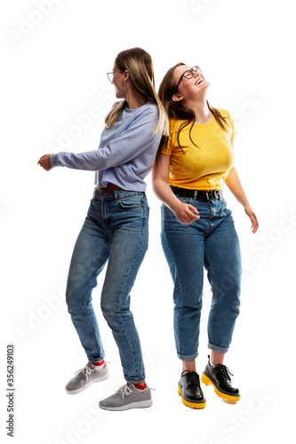 Two laughing dancing young girls in jeans. Friendship and relationship. Isolated on a white background. Vertical.