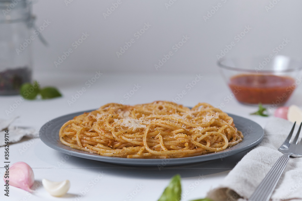Fototapeta premium Spaghetti with tomato sauce and parmesan. Pasta on a white wooden table. Italian dish for lunch.