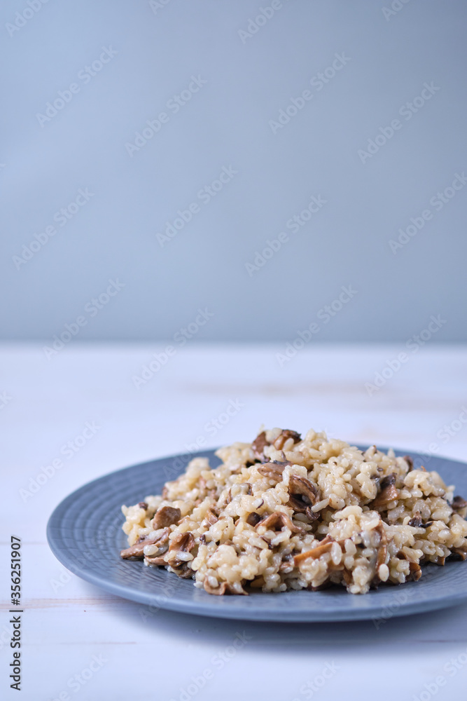 Risotto with mushrooms close-up on a gray plate. Italian dish on a white wooden table.