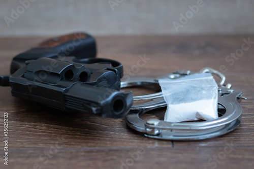 Revolver, handcuffs and bag with white powder on a wooden background. The concept of punishment for drug trafficking. Blurred background. Selective focus. © Vladimir
