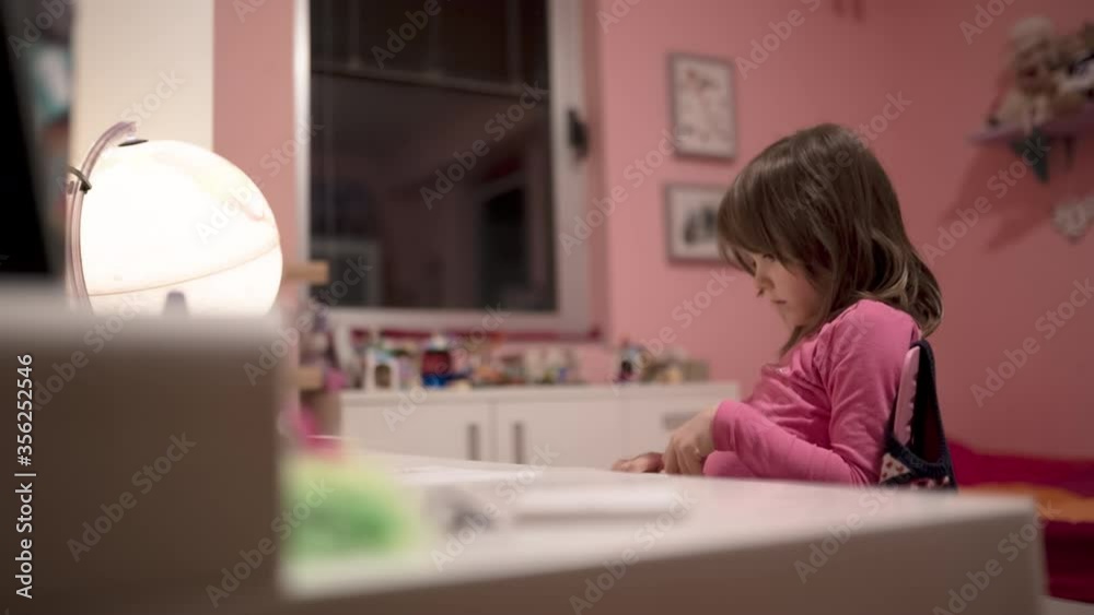Charming little girl drawing and watching tablet with an illuminated globe on a school desk Charming little girl drawing and watching tablet with an illuminated globe on a school desk