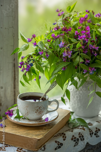 A cup of tea with an old book and a bouquet of forest flowers on a window sill. Retro photo, vintage style.