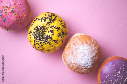 Four donuts with colored glaze on a pink paper background. photo