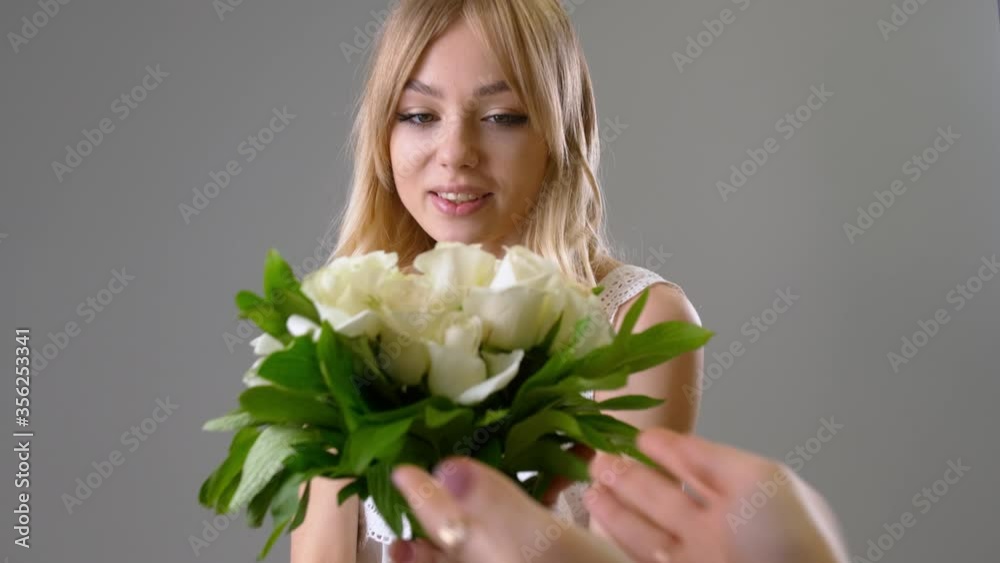 Beautiful young woman receiving bouquet of white roses on grey background Beautiful young woman receiving bouquet of white roses on grey background