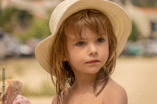 Beautiful little girl with hat eating a doughnut on the beach.