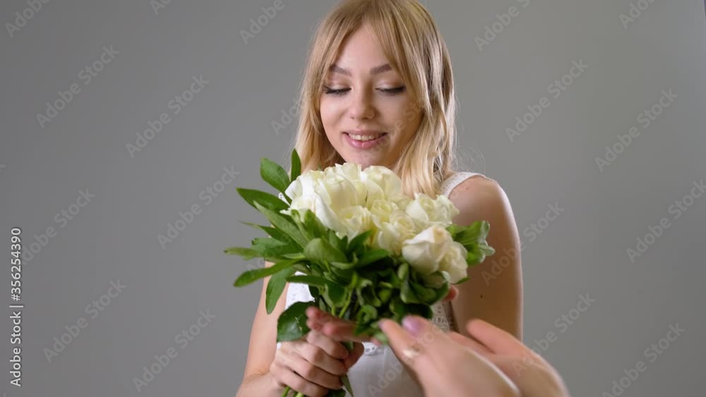 Beautiful young woman receiving bouquet of white roses on grey background Beautiful young woman receiving bouquet of white roses on grey background