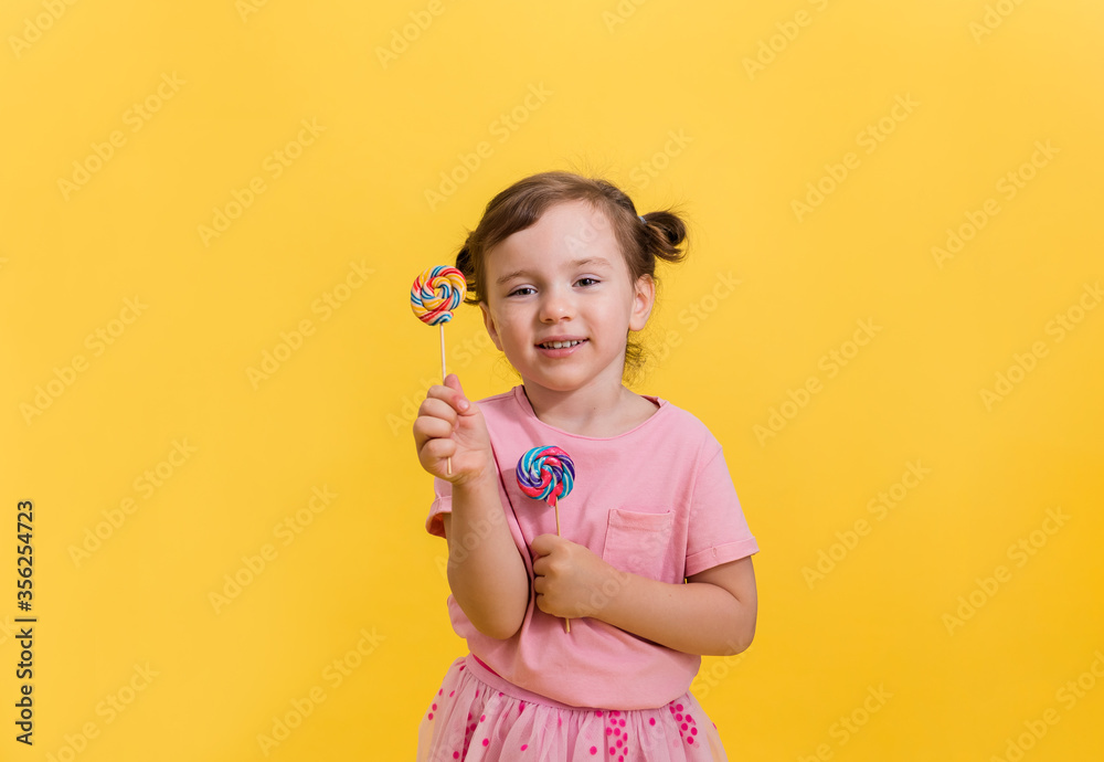 Happy girl with pigtails on a yellow background holding lollipops on a stick Happy girl with pigtails on a yellow background holding lollipops on a stick
