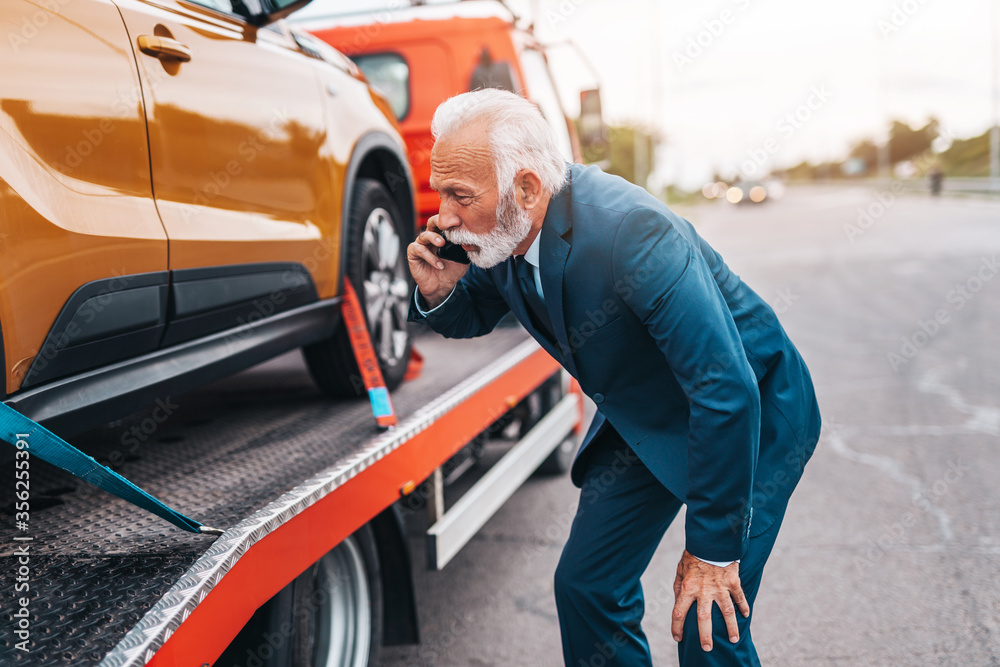 Elegant middle age business man calling towing service for help on the road. Roadside assistance concept.