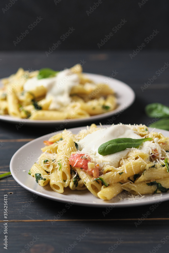 Two portions of pasta with tomatoes, spinach, parmesan and bolognese sauce. Dish in a plate on a wooden table. Two portions of pasta with tomatoes, spinach, parmesan and bolognese sauce. Dish in a plate on a wooden table.