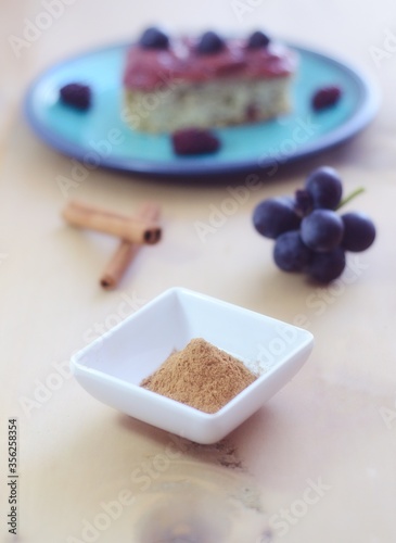 Canela molida fresca en un recipiente blanco lista para ser usada en un postre. Primer plano canela en polvo en un recipiente blanco y en segundo plano frutas y postre de uva sobre una mesa de madera. photo