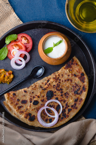 Aloo Paratha / Indian Potato Stuffed Wheat Bread served with Curd & Pickle, Tomato & Onion. Top View on a Dark Moody Background. Traditional North Indian or Punjabi Breakfast. For Food Blog or Menus.