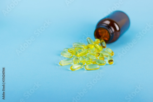 Golden fish oil capsules, omega 3, vitamin D in glass bottle jar isolated on blue background side view. Copy space for your design or text. Health care lifestyle concept.