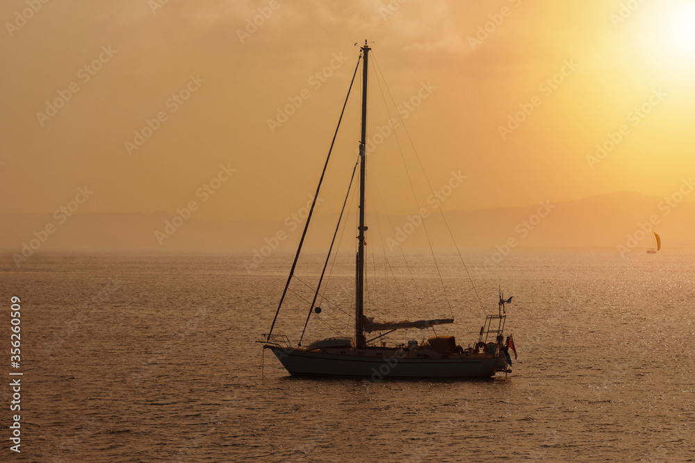 sailing yacht against sunset tinted in warm tones