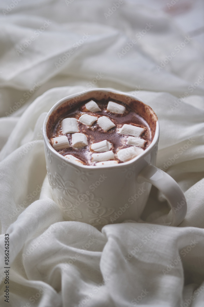 Mug of hot chocolate with marshmallows on a light textile background. White mug of hot drink close-up.