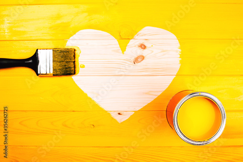 Heart shape of wooden background with brush and open can inside freshly painted yellow surface. Renovation concept. photo