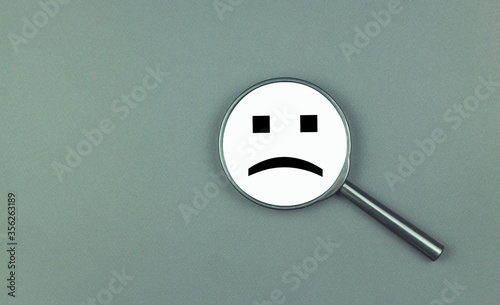 A negative smile is depicted on a magnifying glass. The concept of depression, ill health, failure, frustration, bad luck, anger and defeat.