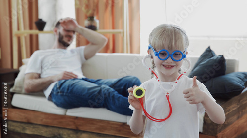 Little cute girl playing as a doctor in the living room. she looking at camera and showing thumbs up