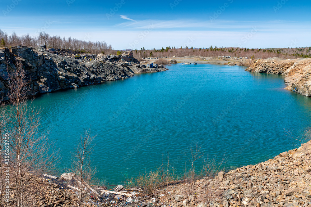 An old quarry filled with water, making it a pond. The water is bluish green, with the sky above.