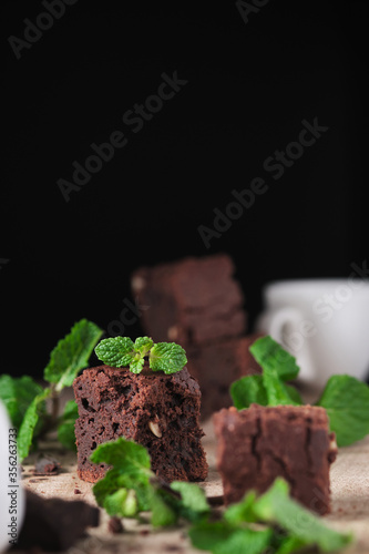 Chocolate brownie with nuts and mint. Sweet and tasty dessert decorated with mint, closeup on a wooden table. Soft focus. photo