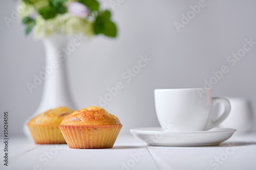 Coffee and fruit muffins with fresh peach for breakfast. Morning table with dessert, espresso and flowers in a vase on a white wooden table.