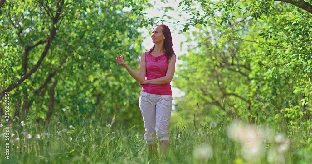 Pretty woman walks through the woods and holds a blade of grass in her hand. Spring walk through the green forest. Woman walks and looks around, she is happy. Pretty woman walks through the woods and holds a blade of grass in her hand. Spring walk through the green forest. Woman walks and looks around, she is happy.