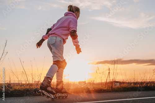 young girl rides roller skates on the road against the background of the sunset