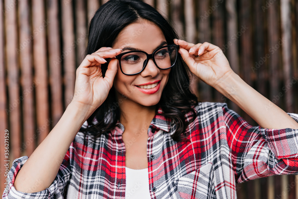 Funny brunette girl looking away and smiling. Outdoor portrait of cute happy woman in glasses wears checkered shirt. Funny brunette girl looking away and smiling. Outdoor portrait of cute happy woman in glasses wears checkered shirt.