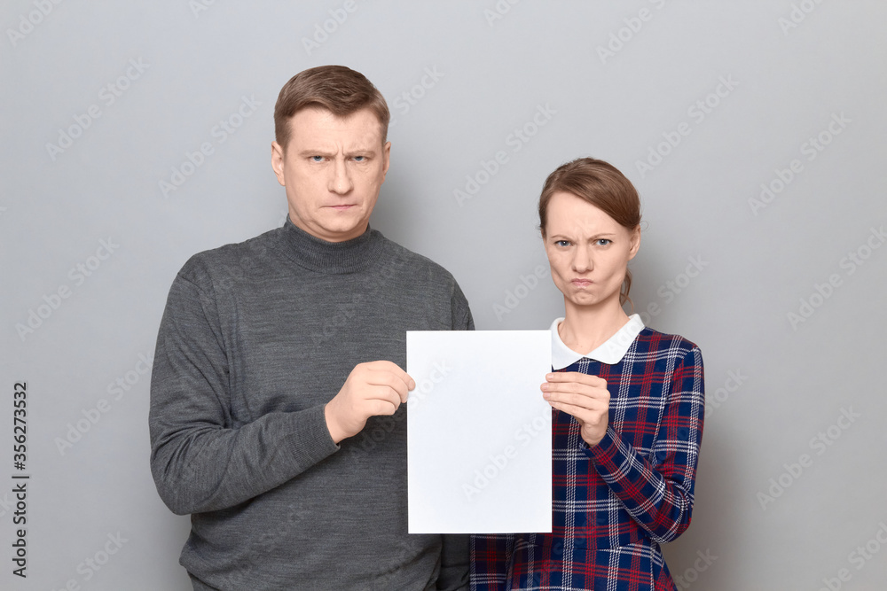 Portrait of adult couple holding together white blank paper sheet Portrait of adult couple holding together white blank paper sheet