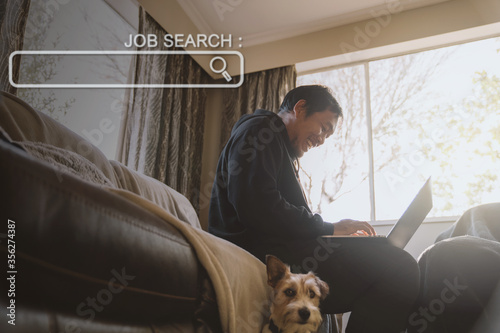 Konstfotografi Asian man in black sitting on couch and searching for jobs by laptop