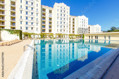 Fototapeta Naklejka Na Ścianę i Meble -  The white buildings of a multi storey luxury residential complex are reflected in the smooth blue water of the pool