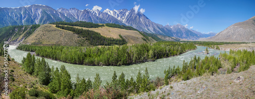 Picturesque valley in the Altay Mountains. The Argut River, greenery along the banks and snow-capped peaks. Panoramic view of the summer landscape.
