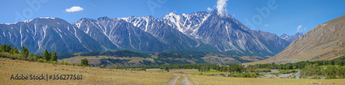 Large panoramic view of the Altay Mountains. The road in a picturesque valley, green forests and snow on the tops. Summer travel in the mountains.