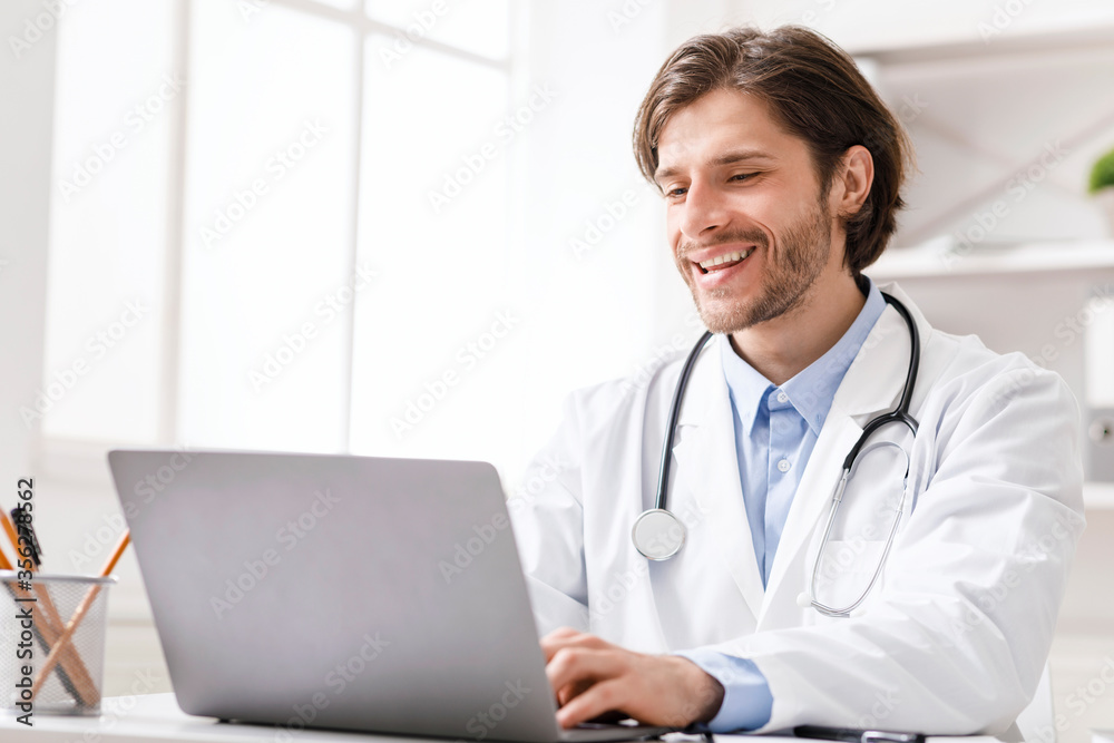 Cheerful doctor working on laptop in office Cheerful doctor working on laptop in office