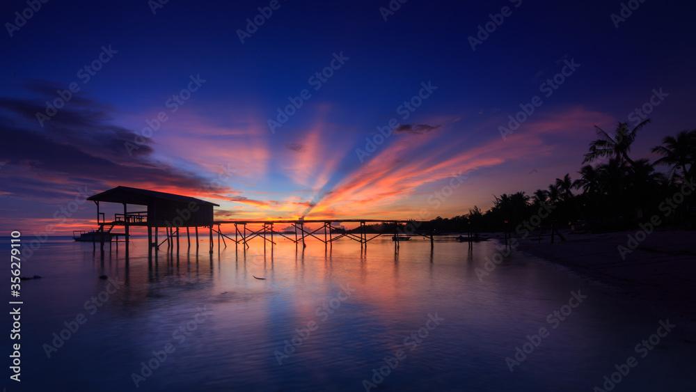 Amazing beautiful sunset with silhouette wooden jetty and coconut tree