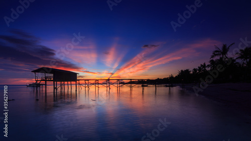 Amazing beautiful sunset with silhouette wooden jetty and coconut tree © alenthien