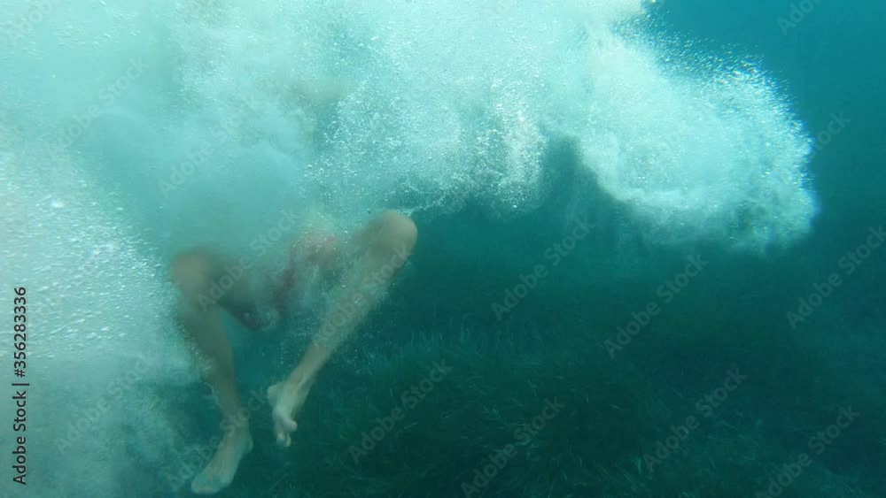 Young man and woman jumping off a sailboat in the Ligurian Sea.