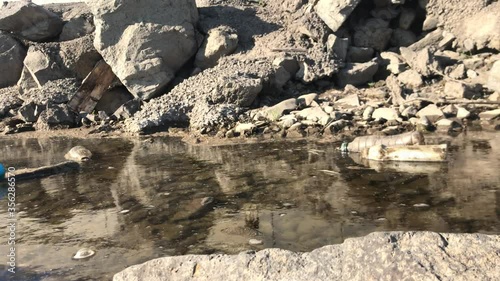 Water pollution. Dirty foam on the water. Also in the water is plastic trash. Bottles from under water. A blue ball floats on water.
